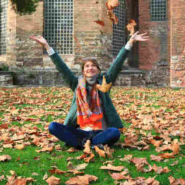 college girl sitting on leaves in yard with hands raised