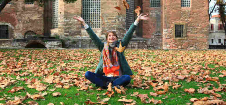 college girl sitting on leaves in yard with hands raised